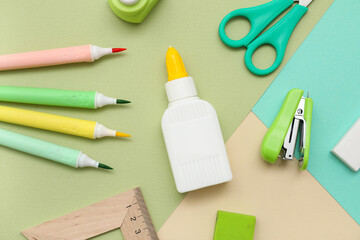 Bottle of glue with felt-tip pens and stapler on colorful background. Top view