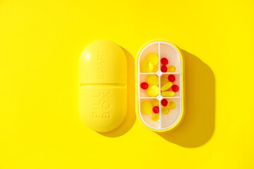 Plastic container with pills on yellow background. Top view