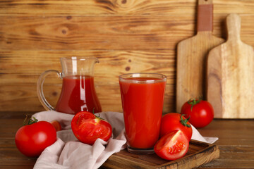 Glass and jug of fresh tomato juice and vegetables on wooden background