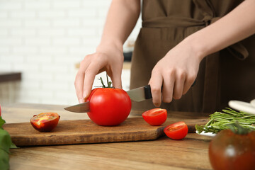 Woman cutting fresh tomato on wooden table in kitchen