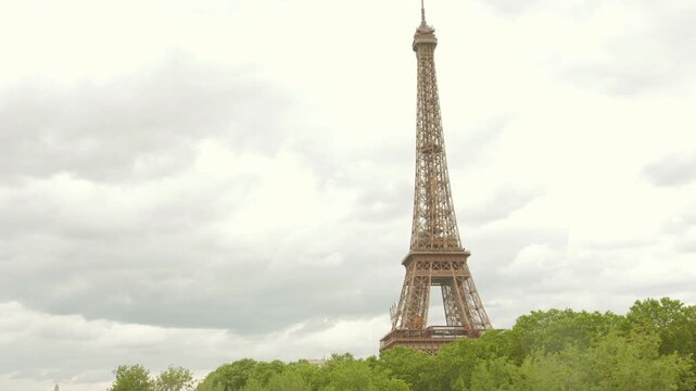 Top portion of Eiffel tower standing tall with trees in the base in a cloudy day.