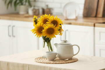 Vase with sunflowers, teapot and cup on dining table in kitchen