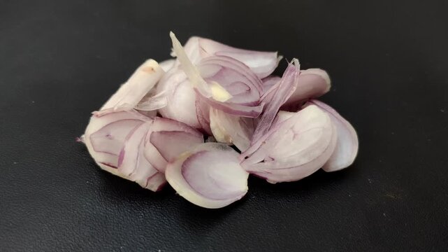 Pieces of fresh red onions or shallots (Allium cepa L. var. Aggregatum) with a black background. That can be eaten raw for cooking spices, pickles, and traditional medicine.&nbsp;