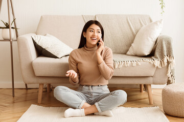 Fototapeta premium Teenage Girl Talking on Phone, Communicating with Friend, Sitting on Floor near Sofa