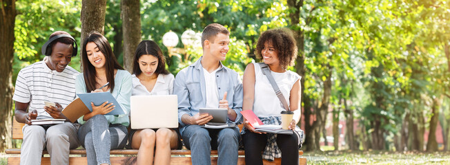 Multiethnic friends studying for exams together outdoors, sitting on bench in campus, having fun together