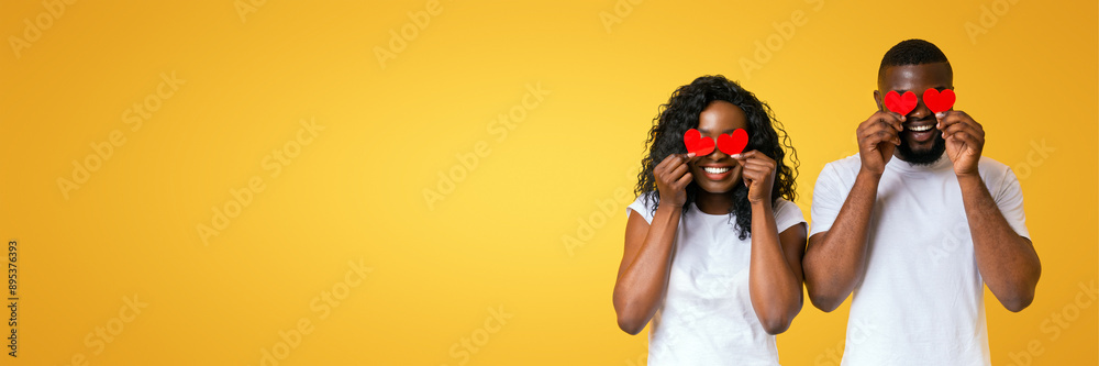 Wall mural African american couple closing eyes with red valentine cards, yellow studio background