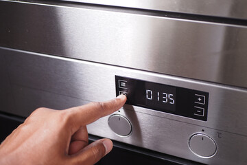 A hand is using a finger to activate the timer button on the control panel of a stainless steel oven
