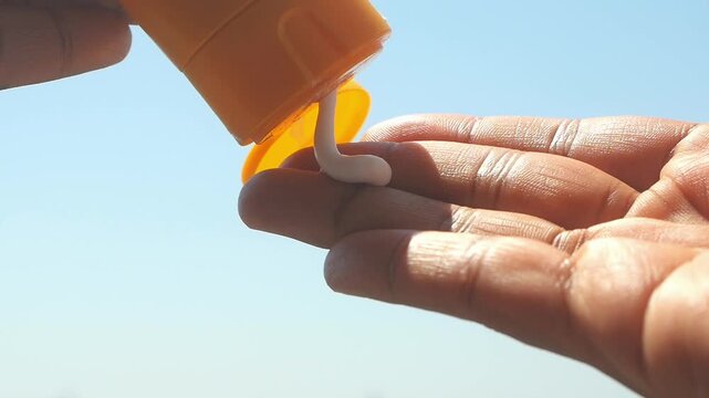 Close up of person hand using sunscreen cream against blue sky 