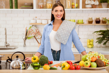 A woman smiles as she prepares a meal in her kitchen, surrounded by fresh fruits and vegetables.