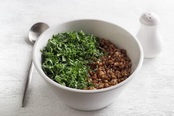 White bowl with boiled buckwheat and kale on a gray background, top view. Healthy homemade vegan food