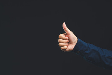 Hand showing thumbs up gesture, positive approval sign against dark background.