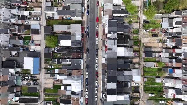 Main street with parking cars in densely populated neighborhood of american town. Sunny day in summer with row of houses and small unkempt lawn in yard. Aerial top down flyover.