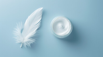 A jar of skincare cream next to a white feather on a light blue surface.