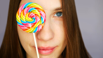 Close-up of a girls face covering her eye with a multi-colored lollipop