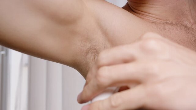 Maintaining fresh underarms throughout the day a crucial step in any morning routine. Here, a man applies deodorant in a well-lit bathroom.