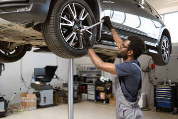 Mechanic wearing gloves fixing car wheel in modern auto repair shop. Car lifted on hydraulic lift...