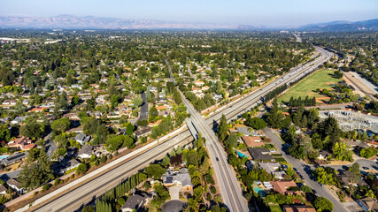 Aerial view of Highway 85 cutting through a residential neighborhood in Saratoga, California, framed by distant mountains surrounding Silicon Valley