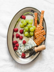 Snack, tapas plate - breadsticks, grapes, cracker, cheese, raspberries on a metal plate on a light surface