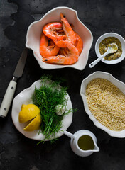 Ingredients for making orzo pasta with shrimp in dill-mustard-lemon marinade on a dark surface