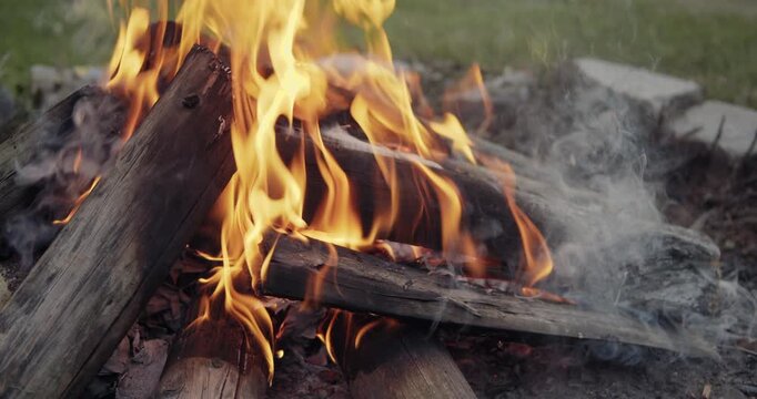 Campfire burning during day, large logs of wood burning with hot flames rising up.