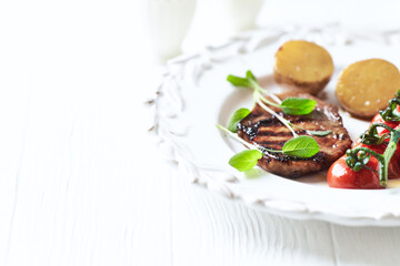 Grilled pork steak with vegetables. White wooden background. Close up. Copy space.	