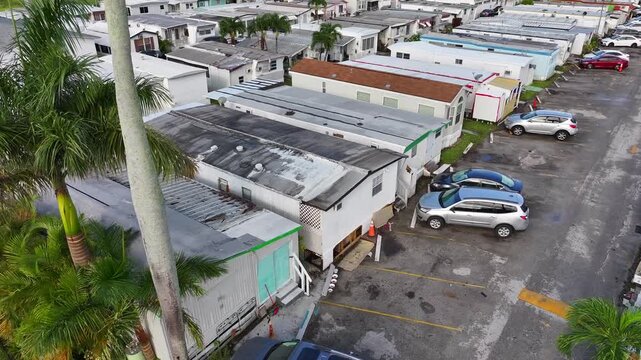 Mobile home park in Florida. Rows of homes and cars. Palm trees and greenery between units. Aerial.