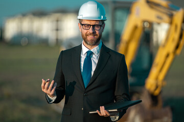 Construction builder manager or supervisor at a construction site. Portrait of construction manager worker in hardhat and suit near excavator. Renovation with construction manager or supervisor.