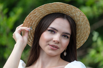 Portrait of a brunette girl in a straw hat outdoors in summer