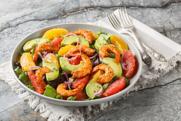 Shrimp salad with citrus fruits such as orange and grapefruit, as well as avocado, red onion and leafy greens close-up in a plate on the table. Horizontal