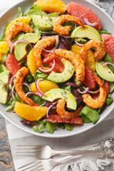 Spicy Shrimp salad with orange and grapefruit, avocado, red onion, arugula and spinach close-up in a plate on the table. Vertical top view from above
