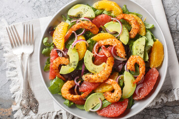 Delicious shrimp salad with oranges, avocado, grapefruit, red onion and leafy greens close-up in a plate on the table. Horizontal top view from above