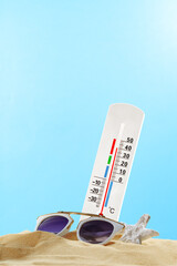 White Thermometer Showing Warm Summer Temperature With Sunglasses On Sand