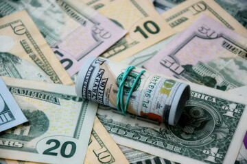 Hundred dollar bills roll lies on big amount of US dollars in different nominations under natural light