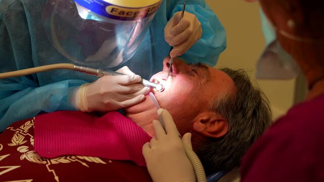 Dentist using dental tools to remove tartar from her patient's teeth