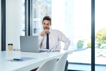 Laptop, planning and thinking with business man at desk in glass office for problem solving or review. Computer, decision and research with corporate employee in workplace for online administration