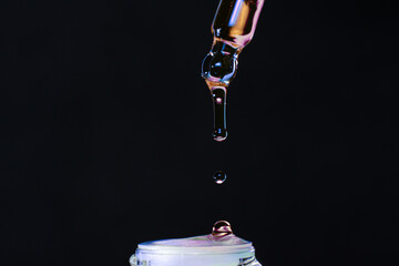 Macro photo of pipette with dripping multicolor liquid on black background, care product.