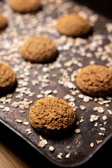 Craft and rustic four oatmeal cookies. Dark food aesthetics, black background with several oat flakes.