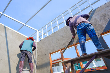 Fototapeta premium 2 construction workers on wooden scaffolding are plastering concrete wall room in house construction site, view from below and perspective view