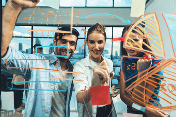 Skilled project manager pointing at glass wall while coworker thinking about plan. Diverse business team working together, brainstorming marketing idea or business plan. Creative start up. Tracery.