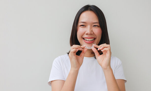 close up young asian woman smiling with hand holding dental aligner retainer (invisible) at dental clinic for beautiful teeth treatment course concept
