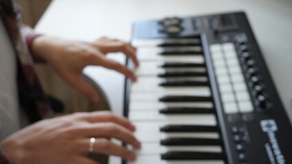 Recording music notes, playing electronic keyboard, midi keys in music sequencer. Hands and midi controller on the table, man composing music, blur