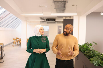 Coworkers walking in modern office;�Woman in traditional Muslim outfit and man�walking and talking in modern office