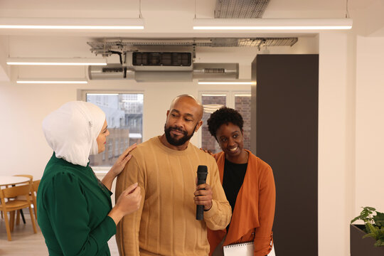 Smiling�multiethnic�creative team members with microphone during presentation in modern studio