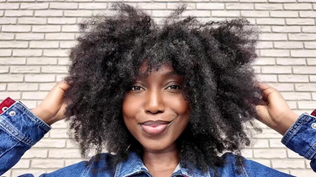 Confident woman flaunts trendy look with afro hairstyle and denim jacket against brick wall backdrop