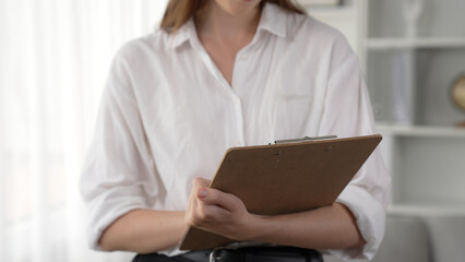 Professional female psychologist with clipboard portrait sitting on arm chair in psychiatrist office or therapy room. Friendly and prim mental healthcare counselor and therapist.