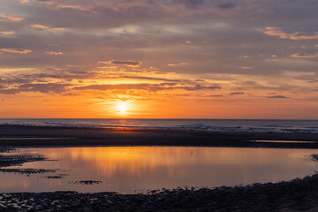 Obraz premium A stunning sunset over a calm ocean, with tide pools and an orange sky, forms a peaceful and serene scene