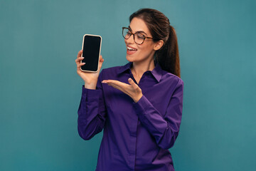 Attractive woman holding smartphone posing in front of camera on isolated blue