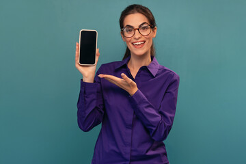 Attractive woman holding smartphone posing in front of camera on isolated blue