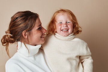 Child in white turtleneck sweater held by woman with red hair in a motherly embrace