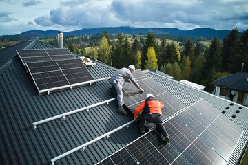 Electricians building photovoltaic solar module station on roof of house. Men technicians in helmets installing solar panel system outdoors. Concept of alternative and renewable energy. Aerial view.